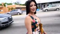 Texas Patti mit tiefem Ausschnitt und Sonnenbrille posiert lächelnd auf einer sonnigen Straße neben einem roten Auto.