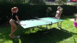 Blonde in engem Top und Shorts beugt sich lasziv über den Gartentischtennis-Tisch, während eine nackte Frau mit gespreizten Beinen zusieht.