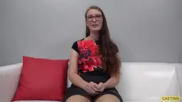 Schüchterne Brünette mit Brille und Blumen-Shirt sitzt brav auf weißer Couch