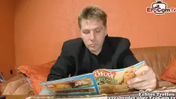 Ein Mann im schwarzen Anzug sitzt auf der Couch und hält lächelnd eine Porno-DVD in den Händen.