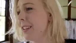 Nahaufnahme einer lachenden jungen Blondine mit zerzausten Haaren und frechem Gesichtsausdruck im Gegenlicht.
