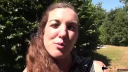 Brünette lacht in die Kamera vor grünen Bäumen